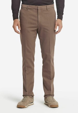 Braune Chino-Hosen aus einer Baumwollmischung mit geradem Bein, ausgestattet mit einem Reißverschluss, Fronttaschen und minimaler Detailgestaltung, kombiniert mit beigen Sneakern.