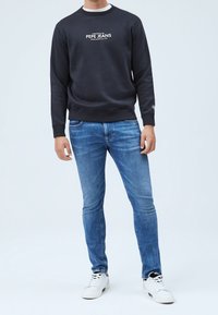 Námořnická mikina s bílým logem "Pepe Jeans", kombinovaná s modrými džíny a bílými teniskami. Ležérní, přiléhavý střih po celé délce.