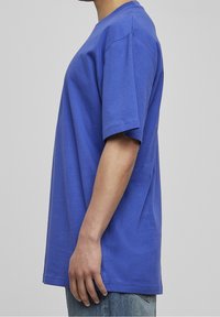 Niebieska bawełniana koszulka z krótkimi rękawami, okrągłym dekoltem i luźnym krojem. Gładka tekstura, prosty dół oraz brak widocznych wzorów lub logo.