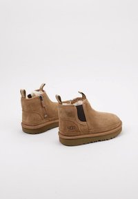 Botas de tobillo de ante marrón con paneles elásticos laterales y una cremallera trasera. Forradas con suave piel de oveja, con suela de goma y marca UGG.