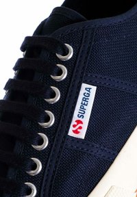 Sneaker in tela marina con punta rotonda, suola in gomma bianca, occhielli argentati e lacci neri. Presenta un'etichetta con il logo sul lato.