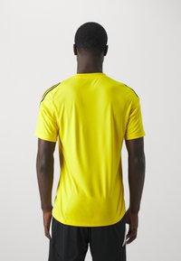 T-shirt de sport jaune à manches courtes, col rond et accents noirs sur les épaules. Fabriqué à partir d'un tissu lisse et léger.