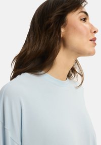 Jasnoniebieska, oversize bluza z okrągłym dekoltem, o miękkiej fakturze i subtelnych detalach w szwie. Luźny krój i obniżone ramiona.