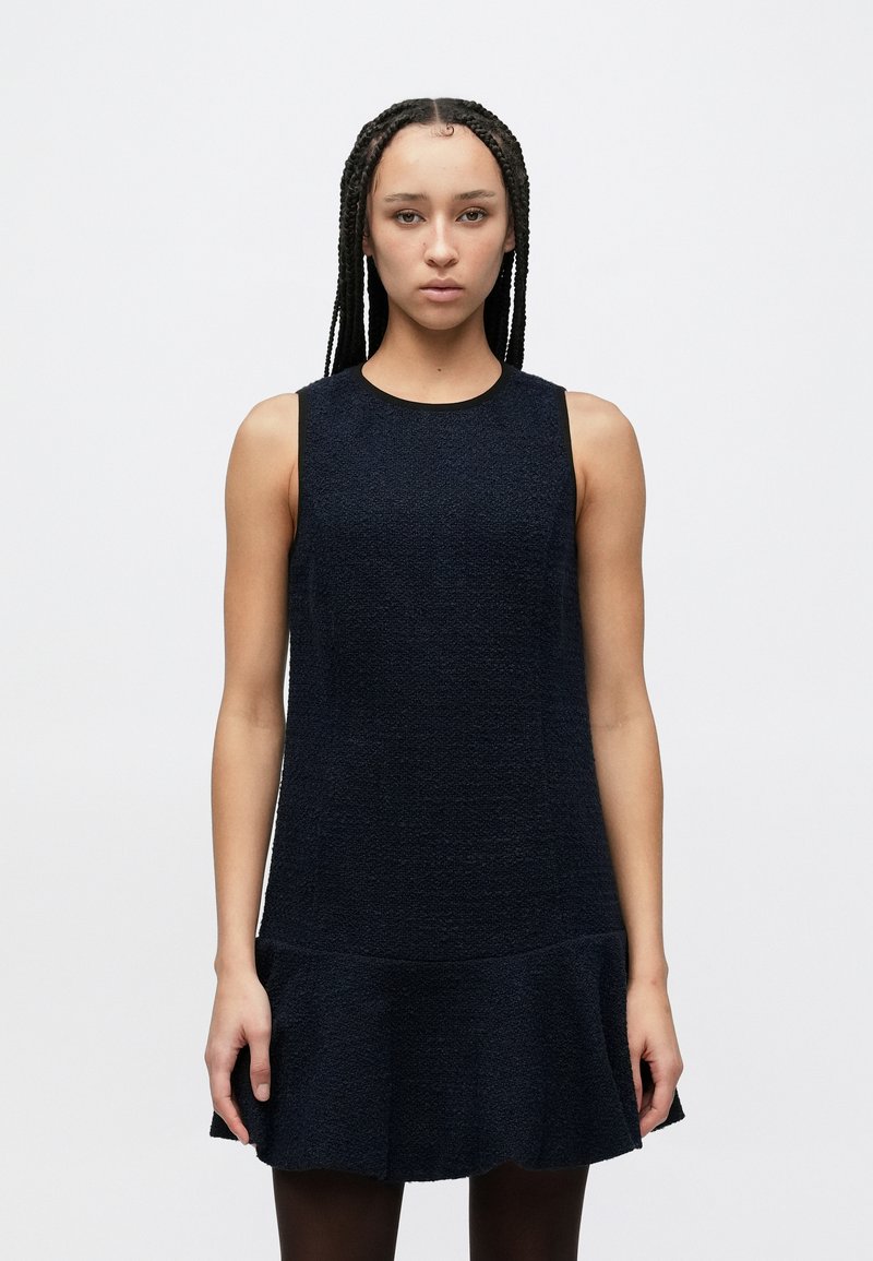 Temno modra obleka z brezrokavnim krojem, okroglim izrezom in nabrano spodnjo robom. Material deluje mehak in rahlo oblikovan.