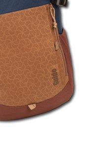 Sac à dos avec un tissu à motif géométrique marron, une section supérieure bleu marine et un fond bordeaux. Comprend une poche zippée et une sangle pour ajustement.