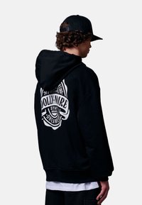 Zwarte hoodie met een witte grafische print op de achterkant, met afgeronde randen, een losse pasvorm en een zachte textuur.