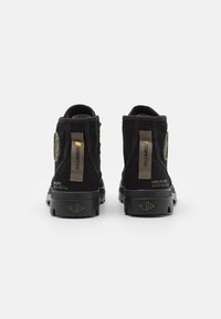 Botines de ante negro con suela de goma, acentos amarillos y un parche redondo con logo. Incluyen talón reforzado y detalle texturizado.