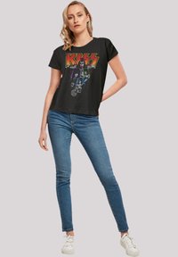 Black cotton t-shirt featuring a graphic print of the band KISS in vibrant colors. Paired with blue jeans and white sneakers.
