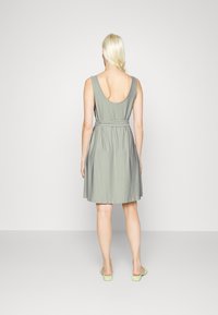 Vestido sem mangas, de tom cinza claro, com corte solto, costas em forma de U e detalhe de faixa amarrada na cintura, feito de tecido suave.