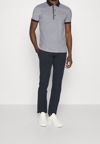 Szary polar z granatowymi akcentami i kołnierzykiem, w zestawieniu z granatowymi spodniami i białymi sneakersami. Posiada logo na piersi oraz paskowany kołnierzyk.