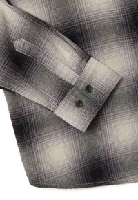 Camisa de cuadros con colores negro, gris y blanco. Presenta una textura de tela suave y dos botones negros en los puños.
