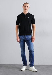 Zwarte polo met korte mouwen, voorzien van een klein logo. Gecombineerd met strakke blauwe jeans en witte sneakers. Eenvoudig, casual ontwerp.