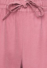 Miękkie, jasnoróżowe spodnie z elastycznym pasem i przewiązaną kokardą. Tkanina wydaje się gładka z delikatną fakturą i prostym krojem.