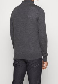 Grå stickad tröja med polo-krage, långa ärmar och ribbade muddar. Baksidan är slät med subtil textur, kombinerad med mörka jeans.