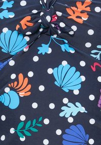Tessuto blu navy con pois bianchi presenta conchiglie e foglie colorate in blu, arancione, verde e viola; dettaglio annodato al centro.