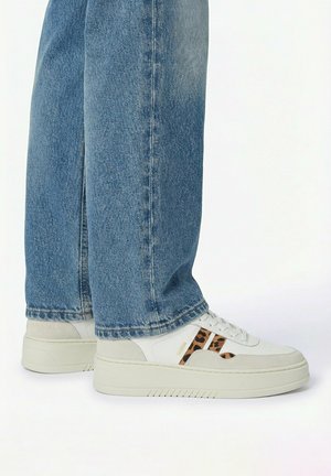 Witte plateau sneakers met luipaardprint accenten gedragen met blauwe wijde pijpen jeans op een witte achtergrond.