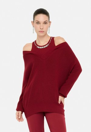 Maglione bordeaux off-shoulder con un tessuto lavorato a maglia, caratterizzato da un design a V e rifiniture in cristallo lungo lo scollo. Vestibilità casual con tasche laterali.
