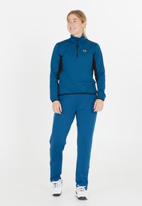 Sininen urheilu paita mustilla yksityiskohdilla, puoliveto kaula-aukko, ja yhteensopivat siniset housut. Yhdistettynä valkoisiin urheilukenkään. Kevyt, sileä kangas.