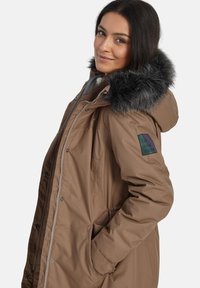 Bruine geïsoleerde parka-jack met een met bont gevoerde capuchon, rits- en drukknoopsluiting, zijzakken en een logo-patch op de linkerarm.