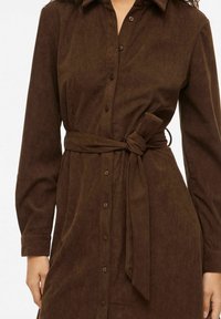 Pruun sametkangast särkkleit pikkade varrukatega, ees nupud ja vööümbrisega. Omadusteks on kraega kaelus ja tekstuuriga kangas.