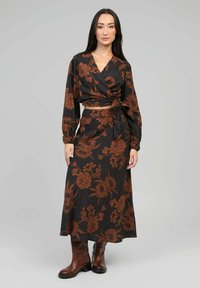 Haut noir à manches longues, orné d'un motif floral marron. Associé à une longue jupe. Porté avec des bottes en cuir marron.