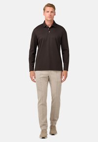 Ilgi piedurkņu melns polo krekls ar trīs pogām, saskaņots ar gaiši bēšiem pieguļošiem biksēm un neitrālu toņu sporta apaviem.