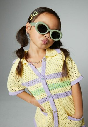Yellow and lavender mesh cardigan with a button front, short sleeves, and scalloped edges. Worn with green sunglasses and a beaded necklace.