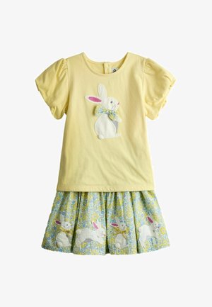 Sárga, rövid ujjú ruha felfújt ujjakkal, fehér nyuszival a mellrészen, virágos masnival, valamint virágos szoknyával, amely több nyuszit ábrázol.