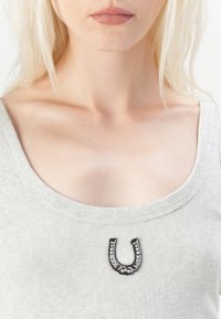 Camiseta sin mangas de color gris claro con un cuello redondeado y un diseño de herradura negra con el texto "BUENA SUERTE". Tejido suave con una forma ajustada.