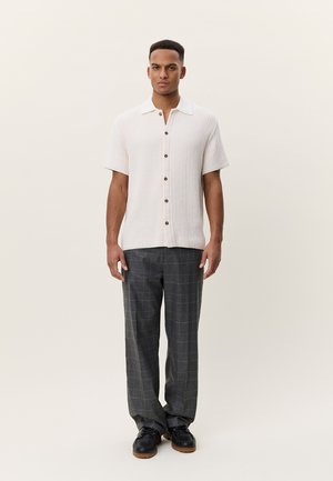 Κοντομάνικο πουκάμισο κρεμ με υφασμάτινη υφή και καφέ κουμπιά, συνδυασμένο με γκρι καρό παντελόνι και μαύρα παπούτσια.