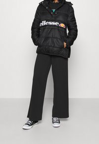 Chaqueta de plumas negra con una banda de logo blanca, combinada con pantalones negros holgados y zapatillas negras. Presenta capucha y bolsillos con cremallera.