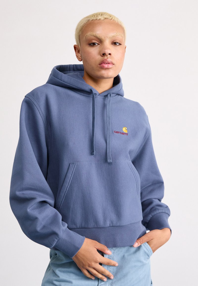 Sweat à capuche bleu clair, en tissu doux, avec une poche avant et un logo brodé en rouge et jaune.