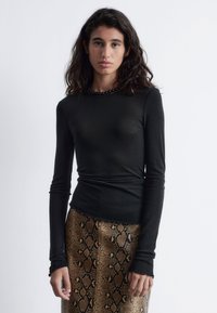 Schwarzes Langarmtop aus weichem Material mit rundem Halsausschnitt und Rüschensaum, kombiniert mit einem gemusterten Rock aus braunem Schlangenhaut.