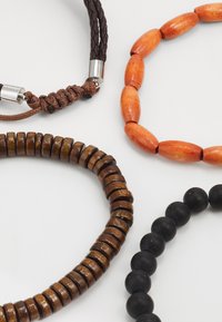 Four bracelets featuring varied materials: a braided brown cord, orange wooden beads, dark wooden discs, and black round beads.