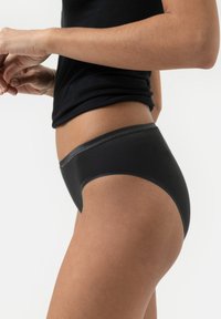 Zwarte katoenen bikiniondergoed met een gladde tailleband en minimale naden, met een strakke, low-rise pasvorm, weergegeven op een lichaam van opzij.