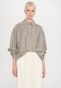 Knappskjorte med et geometrisk mønster i beige og svart. Har spredt krage, oversized passform og rynkede ermer.