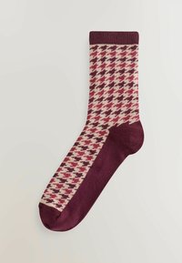 Brūns un krēms houndstooth raksta zeķes ar vienkrāsainu brūnu papēdi un pirkstu. Cauruļveida manšete augšā. Adīta auduma tekstūra.