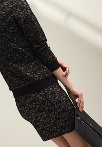 Maglione nero a maglia con motivo testurizzato, abbinato a una gonna aderente coordinate. Include una vita nera e una borsa nera elegante.