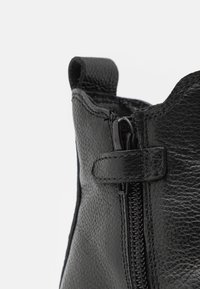 Botín de cuero negro hasta el tobillo con superficie texturizada, cremallera lateral y una pequeña lengüeta en la parte superior para ponérselo con facilidad.