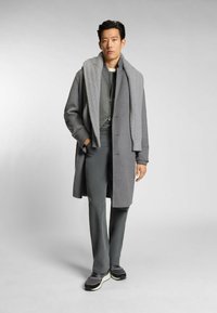 Cappotto grigio in lana con una sciarpa grigia a trama, pantaloni grigi aderenti e sneakers sportive grigie e nere. Design minimalista e colori neutri.