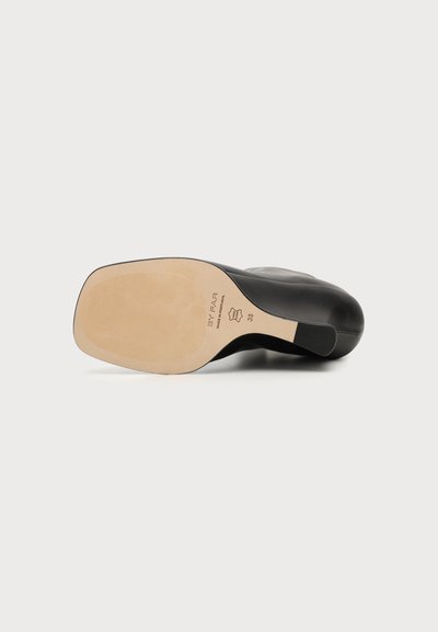 Chaussure en cuir noir vue du côté de la semelle, avec une semelle beige clair, taille 38 et marquages du matériau en cuir.