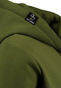 Felpa verde oliva con una texture morbida. Presenta un colletto aderente e un'etichetta nera 'KEY LARGO' sulla cucitura della spalla.
