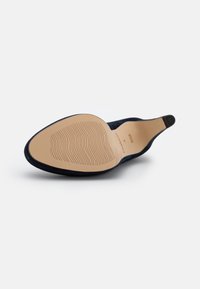 Navy suede high heel shoe with a pointed toe, showing a smooth beige rubber sole featuring a wavy tread pattern and a circular heel cap.