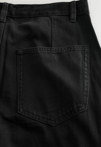 Sorte denim bukser med en synlig baglomme i firkantet form. Stoffet har en tekstureret finish og subtile syninger.