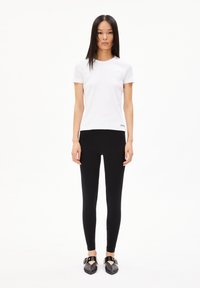 Hvid tætsiddende t-shirt med korte ærmer, parret med sorte leggings og sorte slip-on sko med dekorative metaldetaljer.