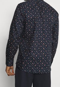 Marinblus med långa ärmar som har små blommönster i röd och gul, tillverkad av mjukt tyg med rundad nederkant och knäppta ärmslut.