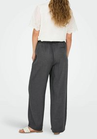 Široké šedé lněné kalhoty s elastickým pasem. Spárované s bílým topem s rukávy z krajky. Jednoduché nazouvací sandály.