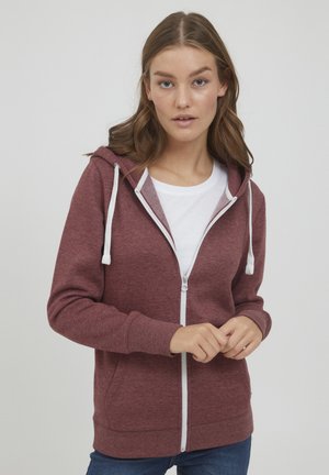 Haut à capuche zippé bordeaux avec des cordons blancs, des poignets et un ourlet côtelés, présentant une texture lisse et une poche kangourou à l'avant. Porté sur une chemise blanche.