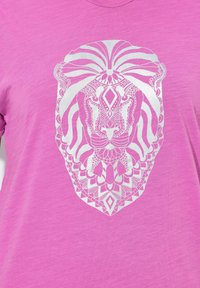 Różowa koszulka z dużą srebrną grafiką lwa, zawierającą skomplikowane wzory liniowe i geometryczne detale, co tworzy teksturowany wygląd.