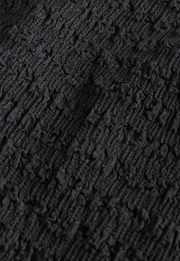 Tessuto scuro con intricati motivi a treccia lavorati a maglia in rilievo che mostrano trama e profondità in una vista ravvicinata.